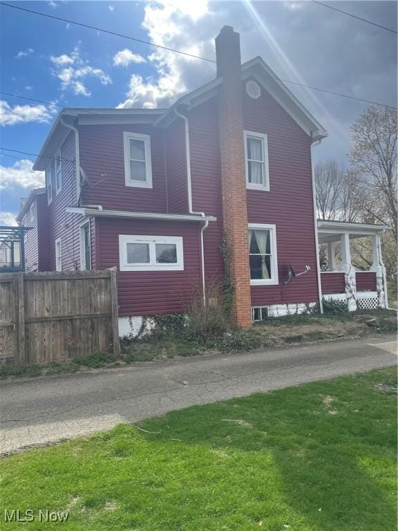 view of property exterior with a chimney, fence, and a lawn