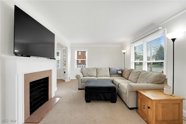 living room featuring light colored carpet, a fireplace with flush hearth, crown molding, and plenty of natural light