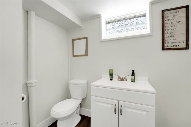 half bathroom featuring toilet, vanity, wood finished floors, and baseboards