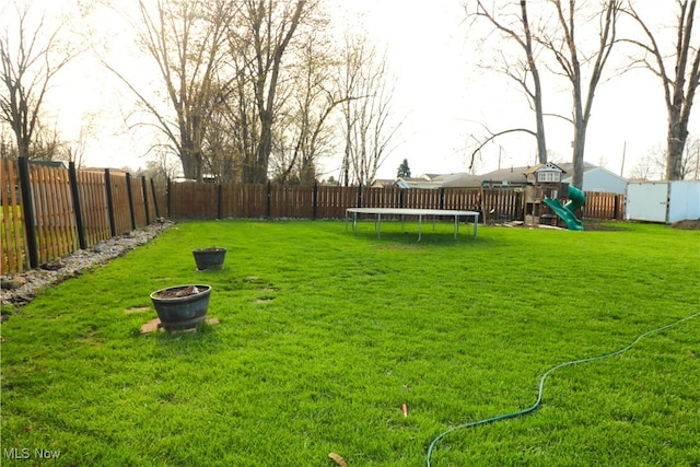 view of yard with a trampoline, a fenced backyard, and a playground