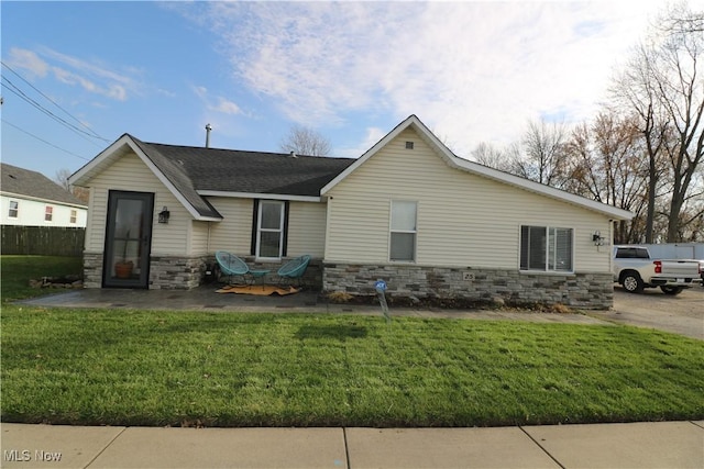 rear view of house with stone siding, a lawn, a shingled roof, and a patio area