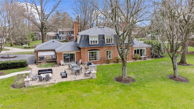 back of house featuring a patio area, a chimney, brick siding, and a yard