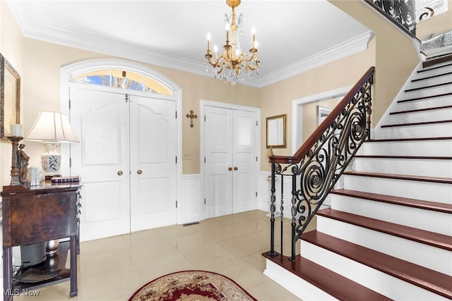 tiled entryway featuring a wainscoted wall, an inviting chandelier, stairs, and crown molding