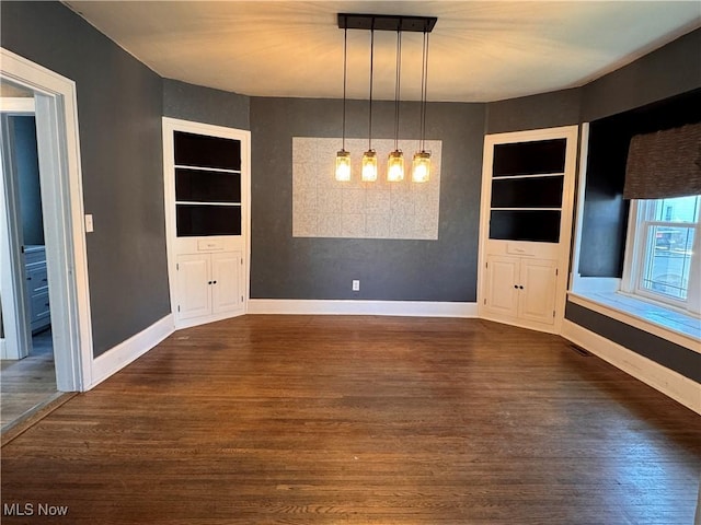 204 N Spring St, Loudonville, OH 44842 - unfurnished dining area with built in shelves, baseboards, and dark wood-style flooring