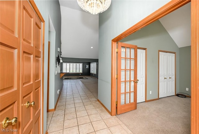 hallway featuring an inviting chandelier, light carpet, light tile patterned flooring, baseboards, and high vaulted ceiling