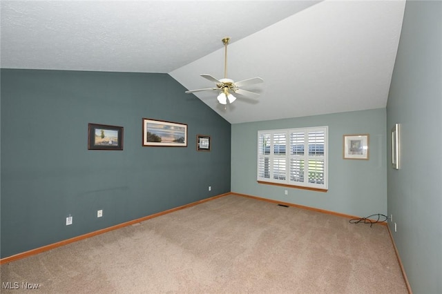 spare room with vaulted ceiling, visible vents, baseboards, light colored carpet, and ceiling fan