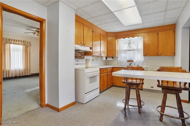 kitchen featuring light countertops, brown cabinets, under cabinet range hood, and white appliances