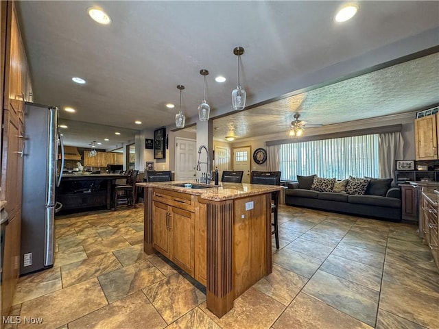 kitchen featuring a sink, a center island with sink, open floor plan, freestanding refrigerator, and a ceiling fan