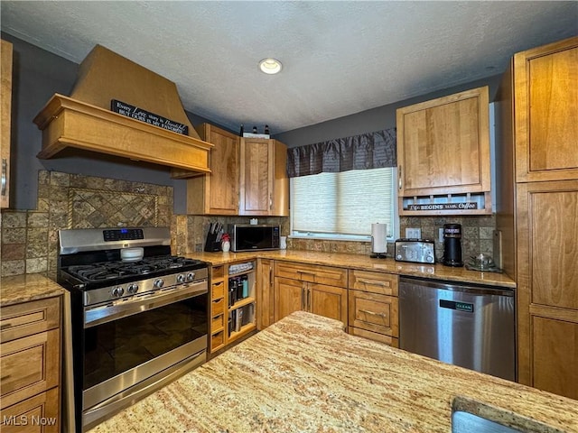 kitchen with brown cabinets, a textured ceiling, appliances with stainless steel finishes, and custom range hood
