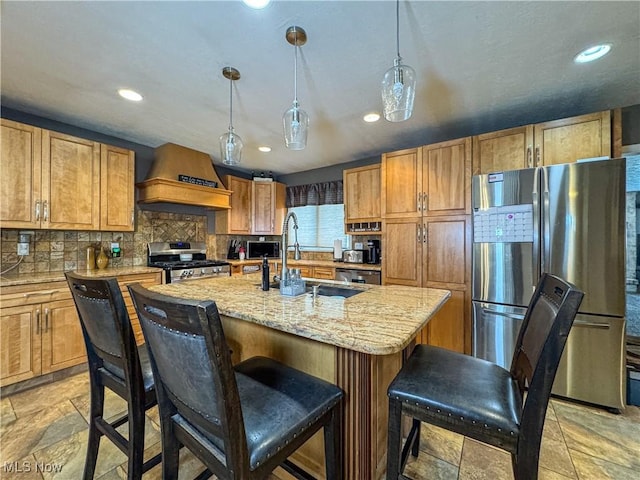 kitchen featuring a sink, stone tile floors, stainless steel appliances, a center island with sink, and backsplash