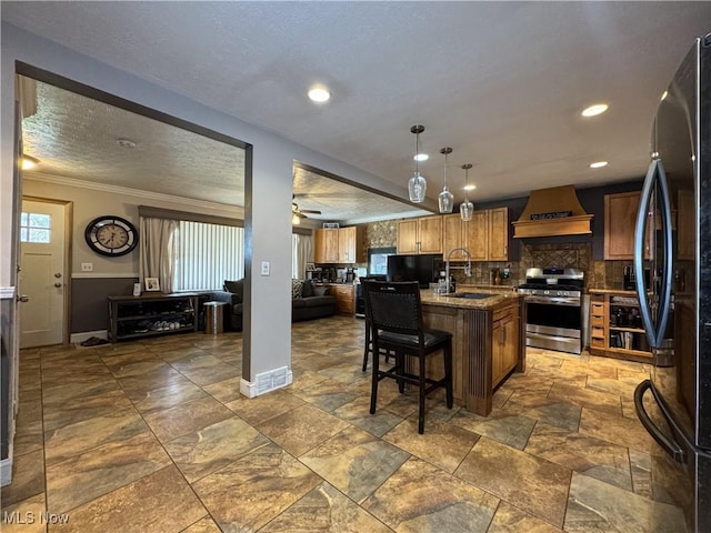 kitchen with backsplash, stainless steel range with gas stovetop, a sink, freestanding refrigerator, and custom range hood
