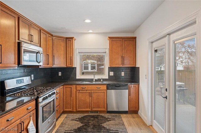 1881 W 65th St, Cleveland, OH 44102 - kitchen with appliances with stainless steel finishes, a sink, brown cabinets, decorative backsplash, and light wood-style flooring