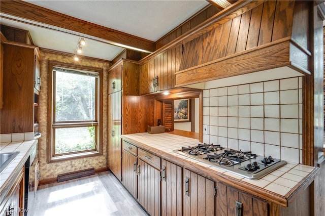 1809 Heritage Cir, Dover, OH 44622 - kitchen featuring light wood finished floors, backsplash, stainless steel gas stovetop, brown cabinets, and tile counters