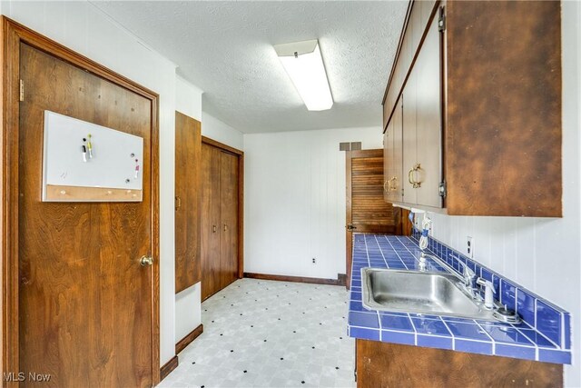 1809 Heritage Cir, Dover, OH 44622 - kitchen featuring a textured ceiling, a sink, baseboards, light floors, and tile countertops