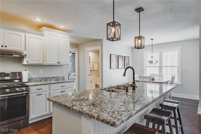 kitchen featuring a kitchen breakfast bar, a sink, stainless steel gas range, white cabinets, and under cabinet range hood