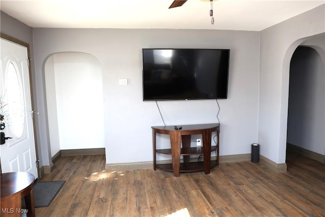 unfurnished living room with baseboards, a ceiling fan, wood finished floors, and arched walkways