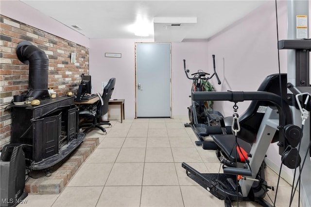 workout room with visible vents, a wood stove, brick wall, and light tile patterned floors