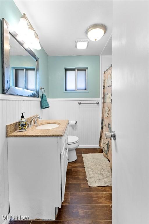 bathroom with a wainscoted wall, wood finished floors, vanity, and toilet