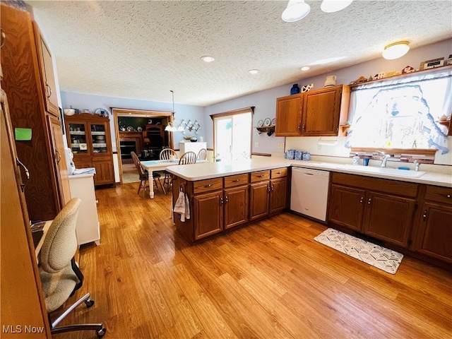 kitchen featuring a peninsula, white dishwasher, a sink, and a textured ceiling