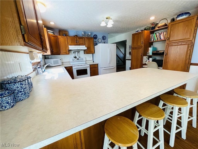 kitchen featuring a sink, white appliances, light countertops, a peninsula, and under cabinet range hood