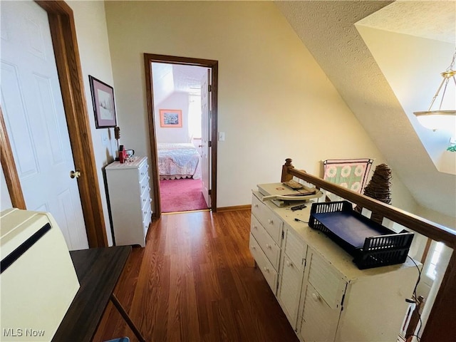 hallway with lofted ceiling, a textured ceiling, dark wood-style floors, and baseboards