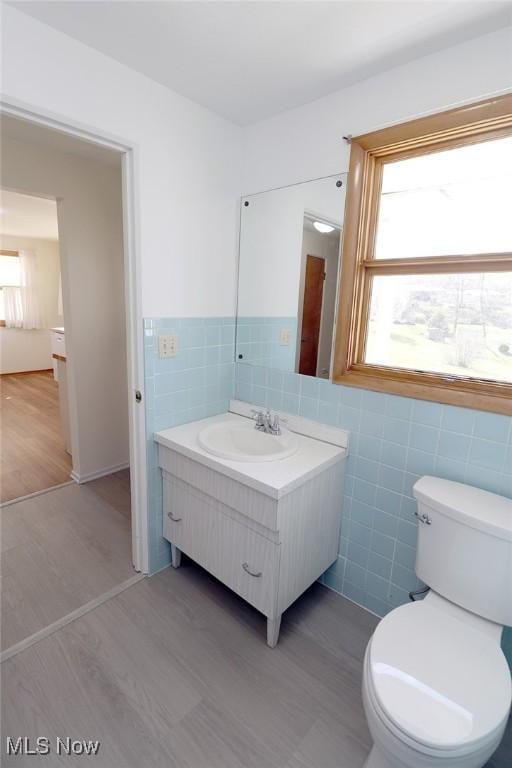 bathroom with toilet, vanity, wood finished floors, and tile walls