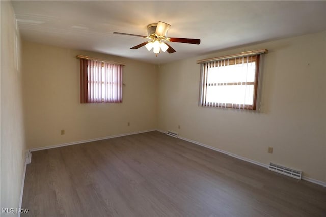 empty room featuring wood finished floors, baseboards, a ceiling fan, and visible vents