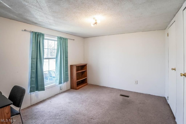 unfurnished office featuring carpet flooring, a textured ceiling, and visible vents