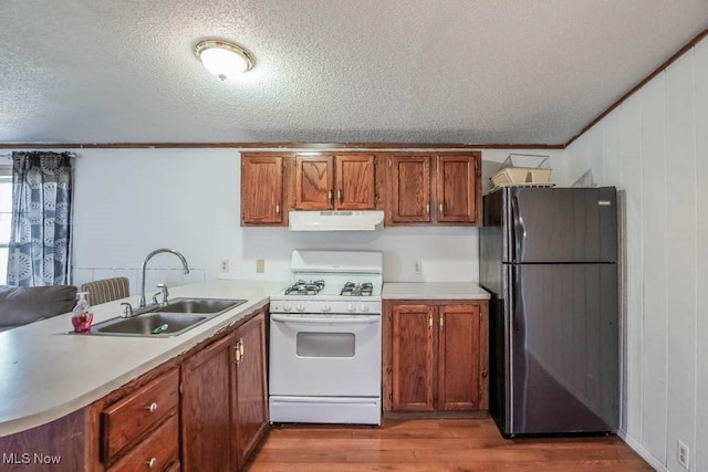 kitchen with a sink, gas range gas stove, freestanding refrigerator, wood finished floors, and under cabinet range hood