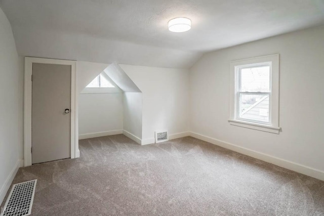 additional living space with vaulted ceiling, a healthy amount of sunlight, carpet flooring, and visible vents