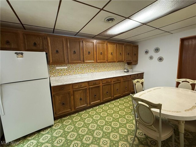 kitchen featuring a drop ceiling, visible vents, freestanding refrigerator, decorative backsplash, and light countertops