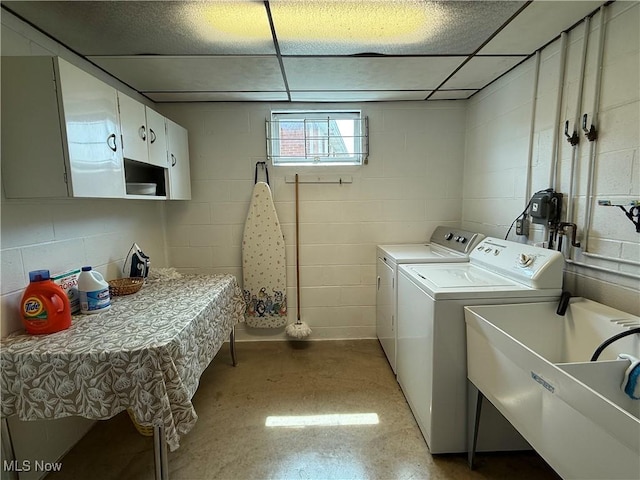 washroom featuring washing machine and clothes dryer, cabinet space, a sink, and concrete block wall