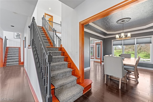 stairs with a tray ceiling, a chandelier, hardwood / wood-style floors, and baseboards
