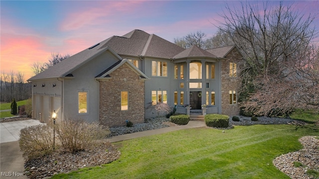 traditional-style house with a lawn, stone siding, concrete driveway, and stucco siding