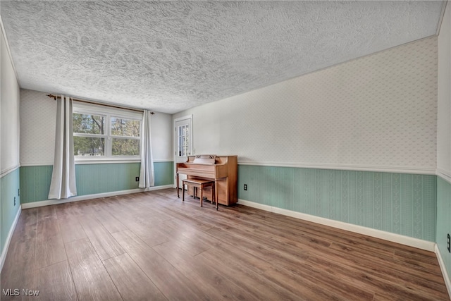home office featuring wainscoting, wood finished floors, wallpapered walls, and a textured ceiling