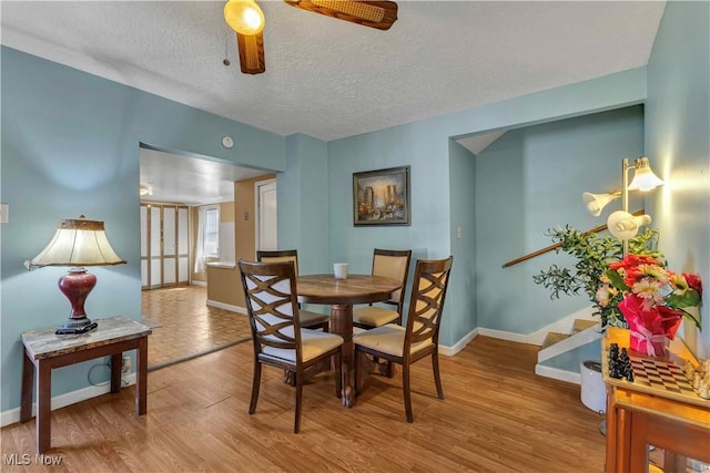 dining area with a textured ceiling, baseboards, a ceiling fan, wood finished floors, and stairs
