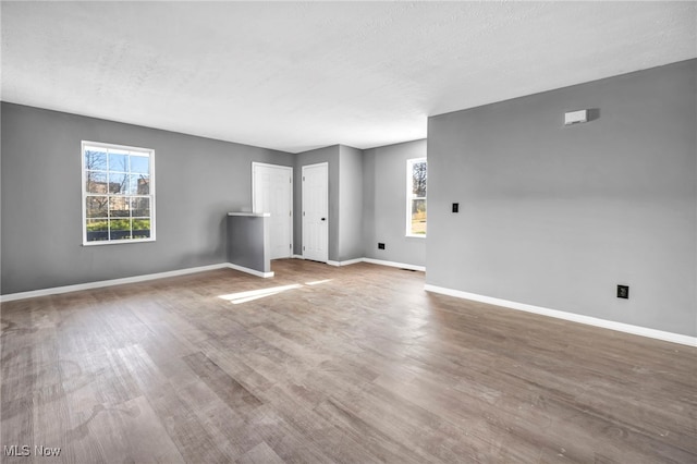 unfurnished living room with baseboards, wood finished floors, and plenty of natural light