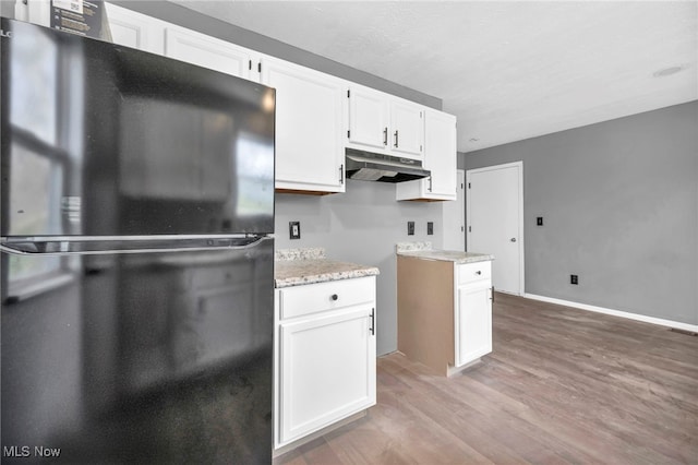 kitchen featuring white cabinets, freestanding refrigerator, light wood-style floors, light stone counters, and under cabinet range hood