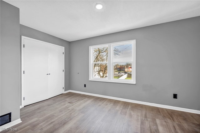 unfurnished bedroom featuring baseboards, wood finished floors, visible vents, and a closet