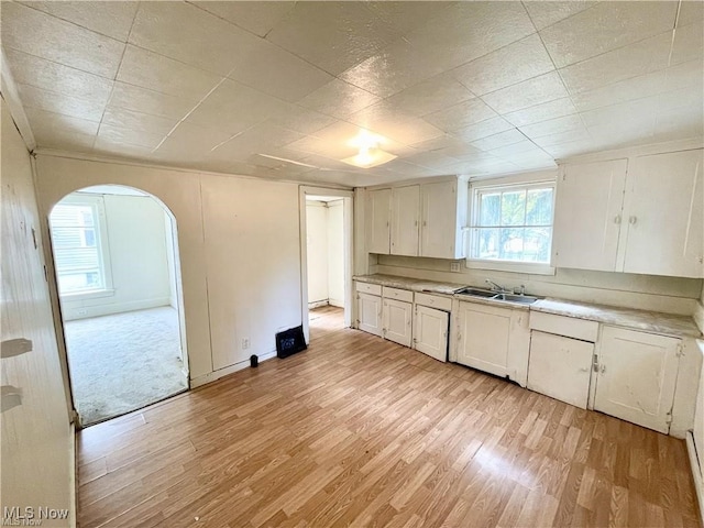 974 Madison Ave, Alliance, OH 44601 - kitchen featuring white cabinets, light countertops, a sink, arched walkways, and light wood-type flooring