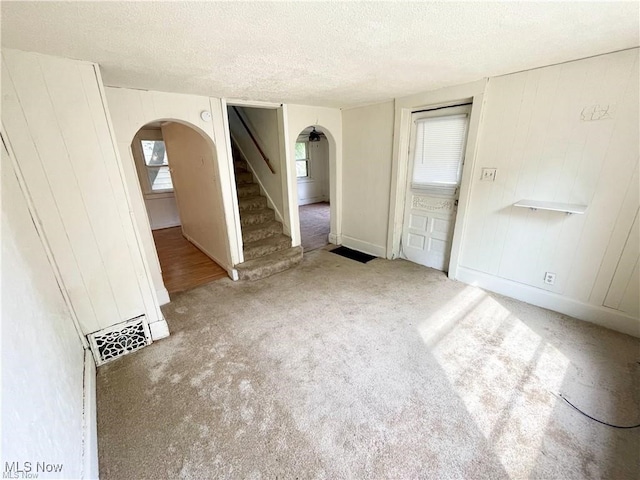 974 Madison Ave, Alliance, OH 44601 - carpeted empty room featuring stairway, a textured ceiling, wooden walls, arched walkways, and visible vents