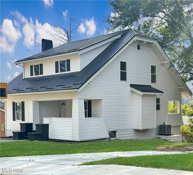 back of property with a chimney, a yard, central air condition unit, a porch, and metal roof