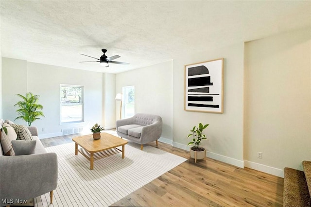 living room featuring a textured ceiling, light wood finished floors, baseboards, and a ceiling fan