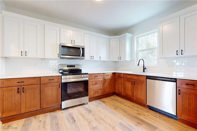 kitchen with stainless steel appliances, light wood-style flooring, a sink, decorative backsplash, and light countertops