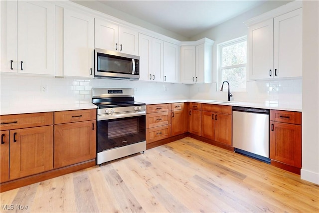 kitchen with appliances with stainless steel finishes, tasteful backsplash, a sink, and light wood-style flooring