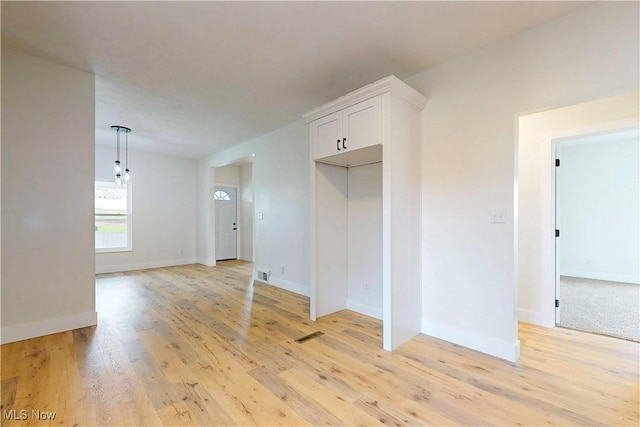 spare room featuring light wood-type flooring, visible vents, and baseboards