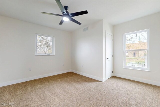 spare room with light colored carpet, ceiling fan, baseboards, and visible vents