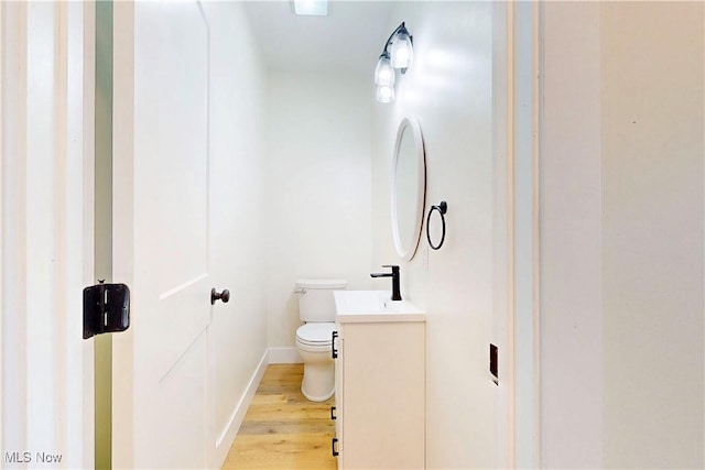 half bathroom with baseboards, wood finished floors, toilet, and vanity