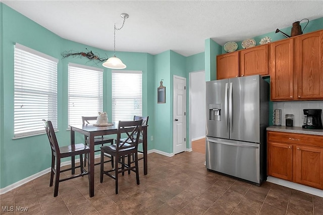 kitchen with baseboards, brown cabinets, stainless steel refrigerator with ice dispenser, light countertops, and hanging light fixtures