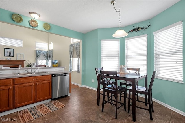 kitchen with brown cabinets, a wealth of natural light, stainless steel dishwasher, and a sink